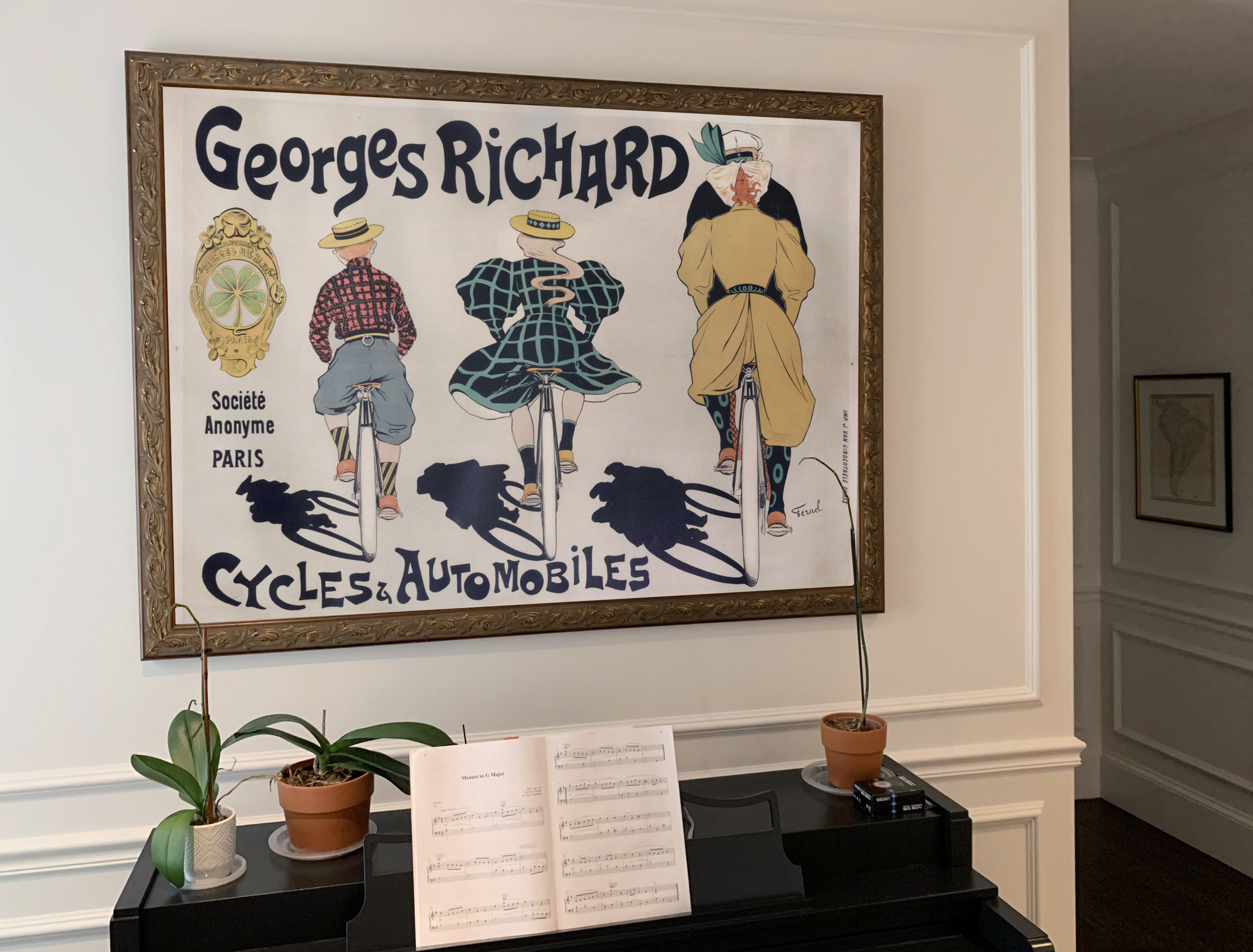 Piano with music and plants on top with poster with cycles hanging above. 